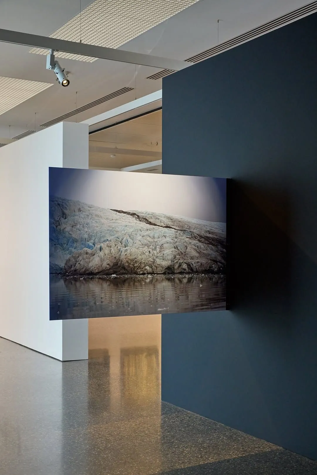 Large glacier photograph on a deep blue wall above a mechanically polished concrete floor at Murray Art Museum Albury