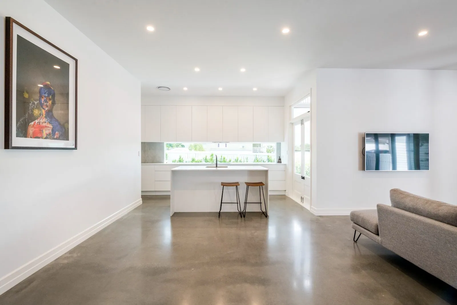 Minimalist open-plan living and kitchen with a warm grey polished concrete floor