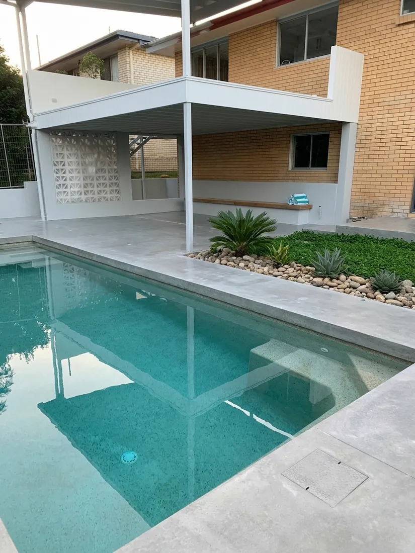 Honed concrete lap pool surround beside a Brisbane home with rock garden