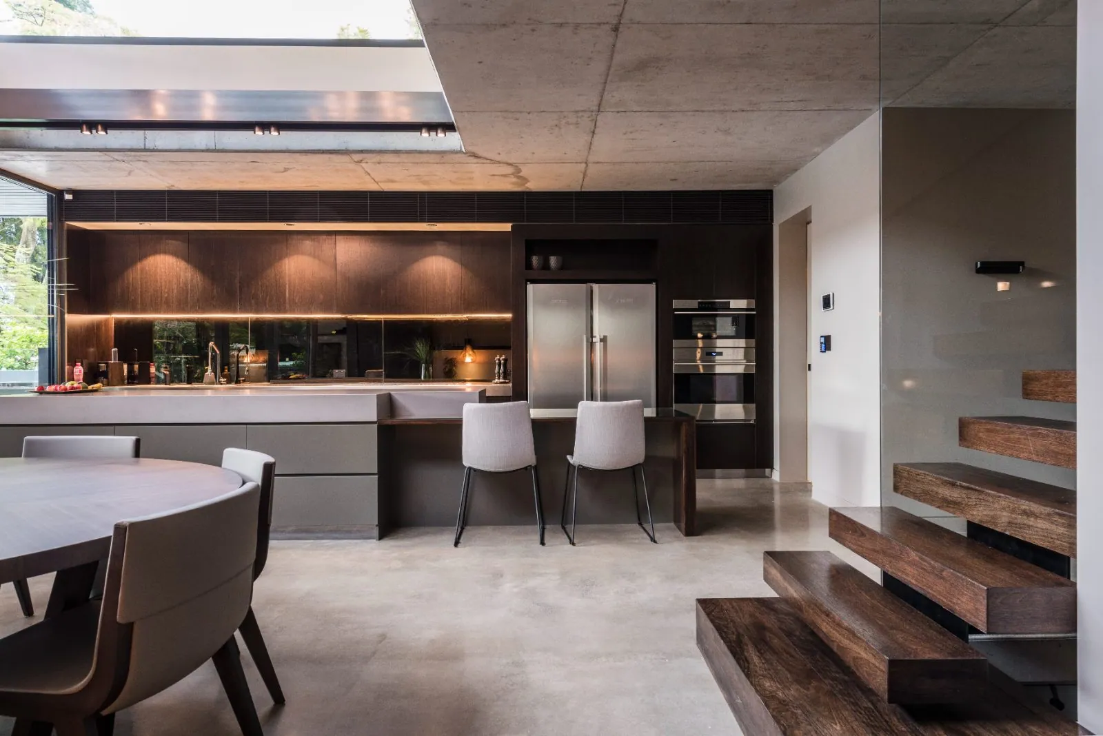 Dark contemporary kitchen and timber stair over a mid-grey polished concrete floor
