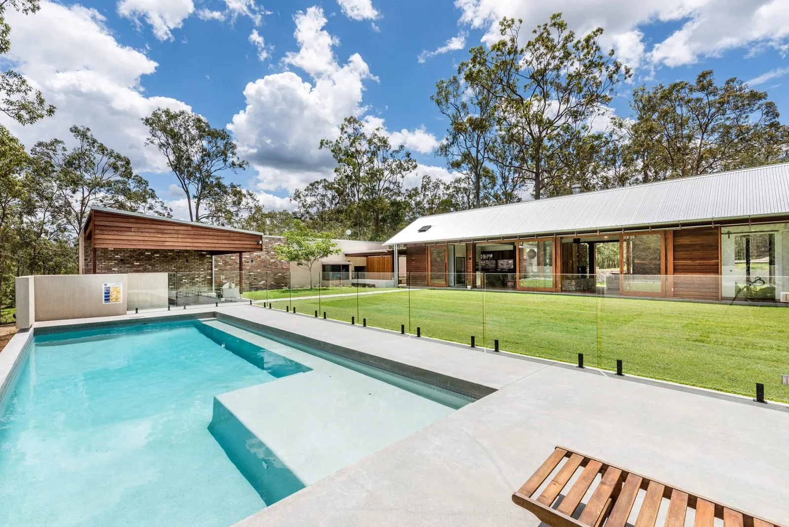 Honed concrete pool surround with glass fencing at a modern acreage home near Brisbane