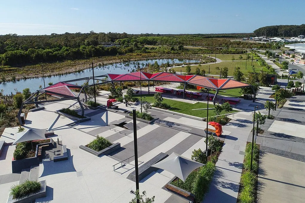 Honed concrete plaza with red shade sails and patterned outdoor polished concrete at Baringa Town Centre