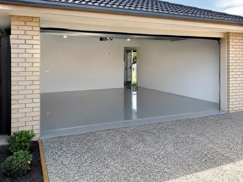 Solid colour epoxy garage floor Brisbane Grey solid colour epoxy garage floor opening onto an exposed aggregate driveway in Brisbane