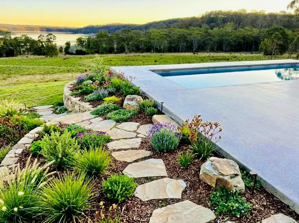 Honed concrete infinity edge pool surround with rock garden landscaping and rural views at sunset, Gold Coast