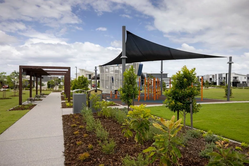 Honed concrete path beside a shade sail playground in the Stockland Aura parkland, Bells Creek