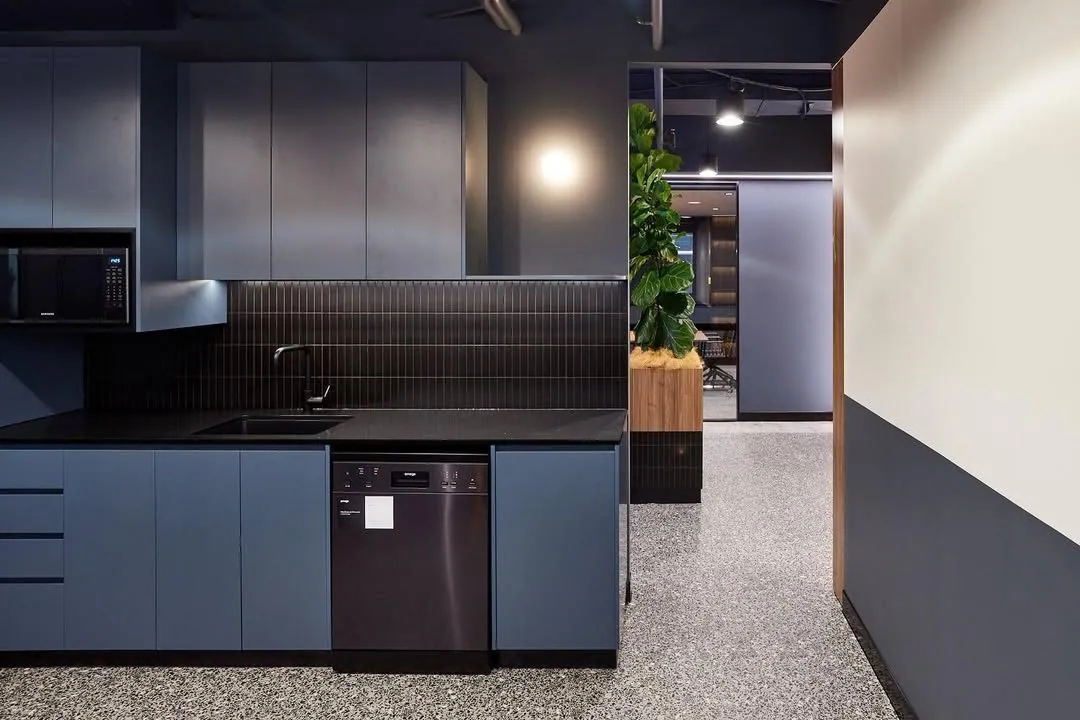 Grind and seal polished concrete floor in an office kitchenette with blue joinery and a black tiled splashback at the Archway commercial office fit-out, Brisbane