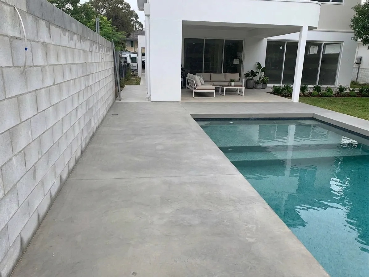 Smooth honed concrete pool surround with minimal stone exposure beside a modern home