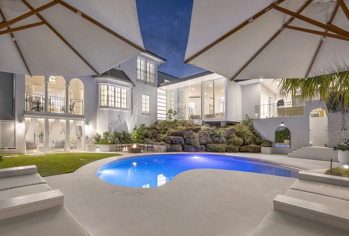 Honed concrete pool surround around a kidney-shaped pool at a Hamilton home in Brisbane at dusk
