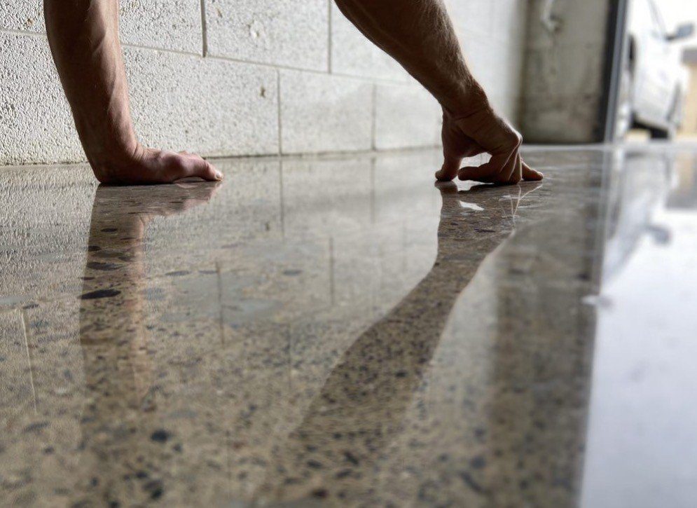 Close-up of hands finishing a high-gloss polished concrete floor with exposed aggregate, Brisbane