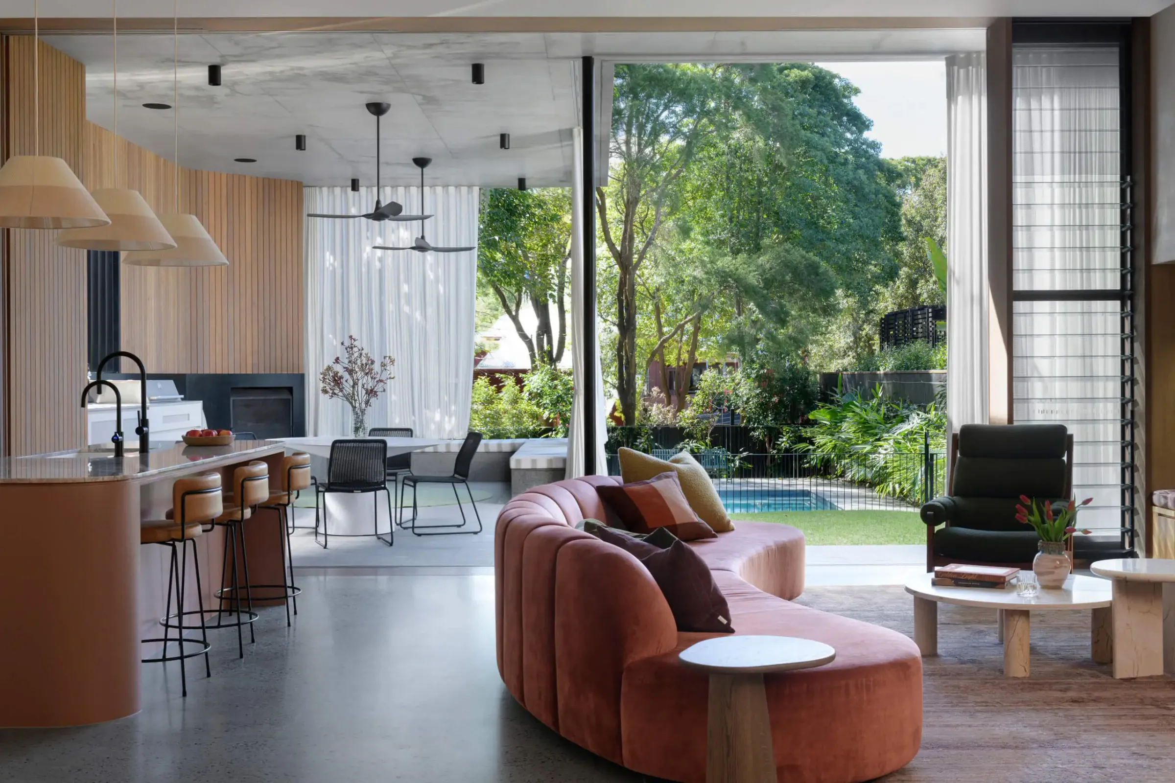 Open-plan living and kitchen with polished concrete floor opening to a leafy garden and pool, by OzGrind